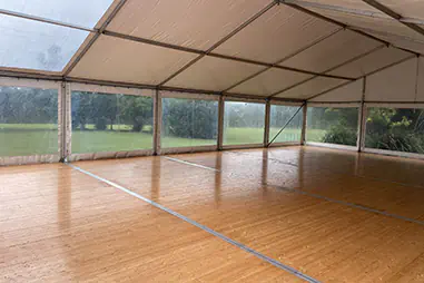 Integrated marquee flooring with timber-style panels, clear side walls, white roof lining and open lawn views outside