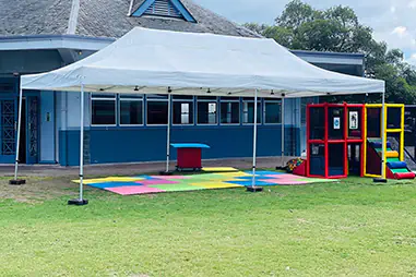 White pop-up canopy set up outside a school building with colourful soft play mats, play equipment and open lawn space