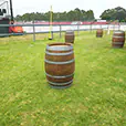 Timber wine barrels spaced across an outdoor event lawn beside stadium seating and fenced entertainment area