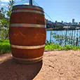 Wooden wine barrel styled as a cocktail table positioned outdoors near a river with city skyline and bridge in the background